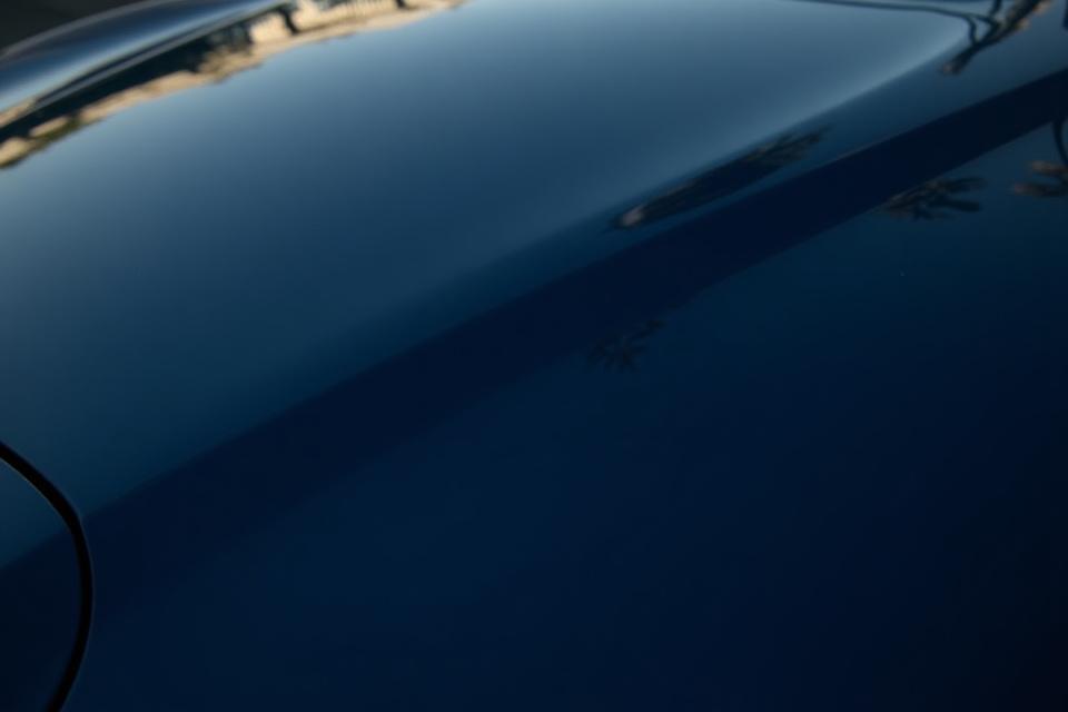 Egy ragyogóan tiszta, sötét színű autó motorházteteje, tükröződő felülettel. A fotó az autótisztaság fontosságát hangsúlyozza.